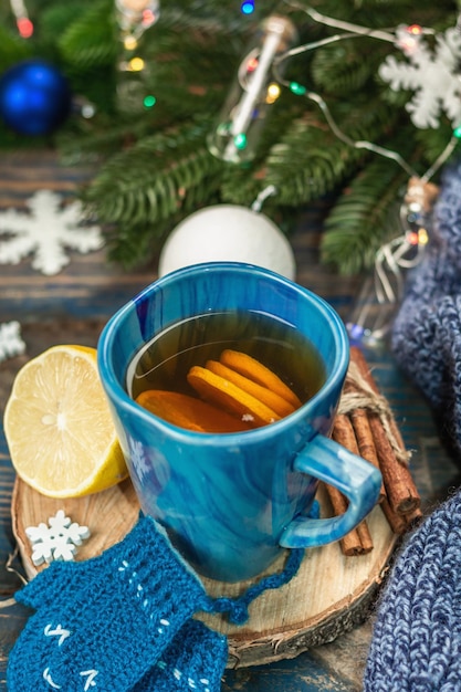 Hot drink with crocheted funny mittens. Traditional winter decor, fir tree branches, snowflakes. Festive seasonal arrangement in blue tones, old wooden background, close up