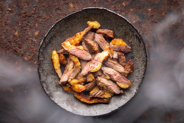 Hot juicy sliced grill beef fillet steak meat in wabi sabi style plate on rusty texture background with somke, top view