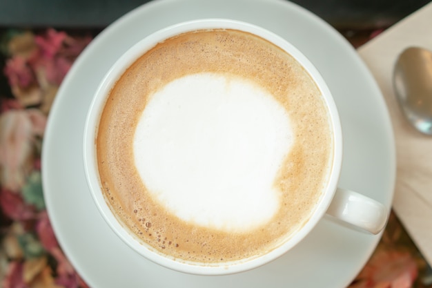 Hot latte art coffee in white cup with metal spoon blurred background