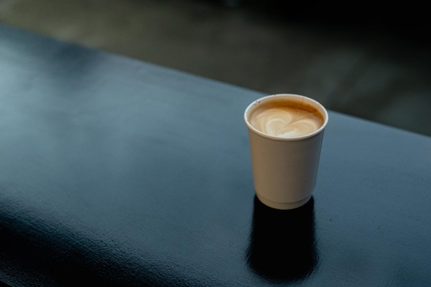 A hot latte coffee served in a paper cup on a black table at a coffee shop.