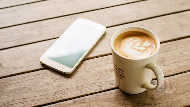 Hot latte coffee and smartphone on a wooden table.