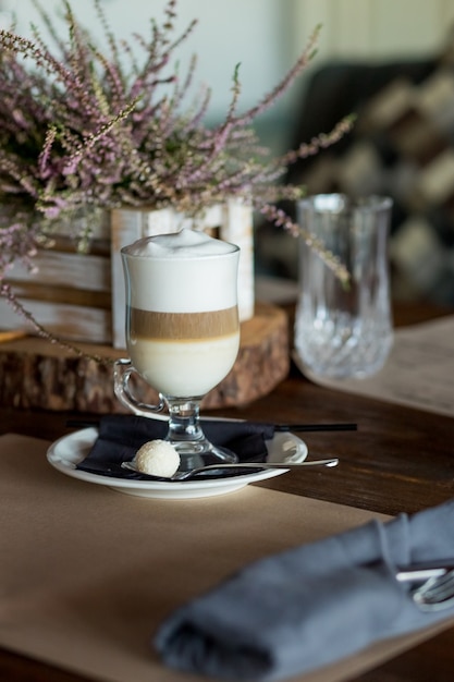 Hot latte macchiato coffee with tasty foam clear glass on dark wooden table serving with cookie,cane sugar. Coffee time, delicious sweet drink.Breakfast time. Retro toned image. Low key dark photo.