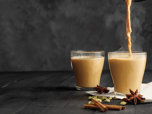 Hot masala tea is poured into a glass glass. Steam comes out of the mug. Gray background.  