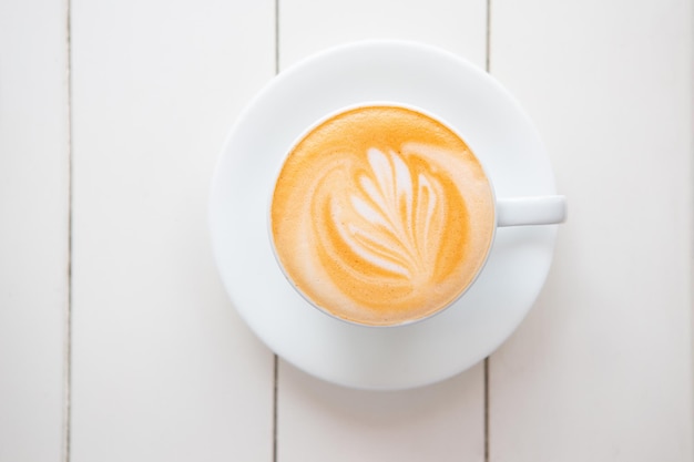 Hot milk tea with latte art in white cup on white wooden table