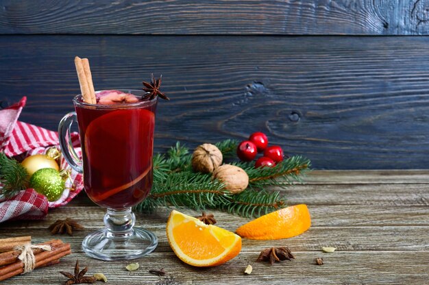 Hot mulled wine in glass mug on a wooden table. Fragrant traditional winter drink based on wine, juice, spices, seasonings, fruits.