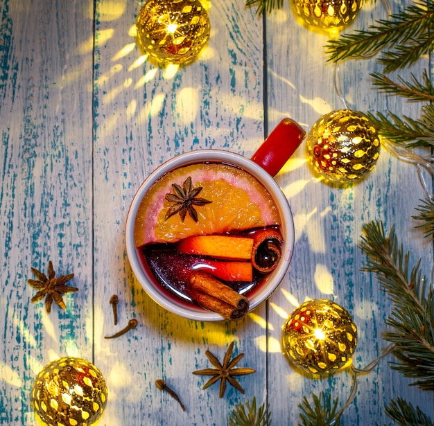 Hot mulled wine with orange, anise and cinnamon on the background of Christmas tree branches and garland. Warming Christmas drink.