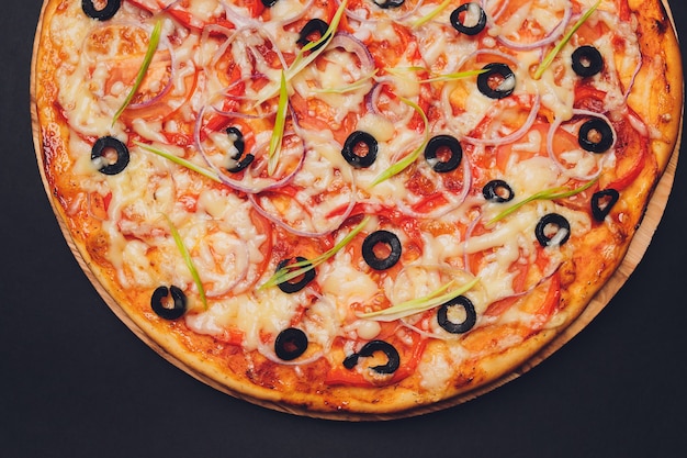 Hot pizza with Pepperoni Sausage on a dark background with copy space. Pizza with mushrooms, tomatoes, cheese, onion, oil, pepper, salt, basil, olive.