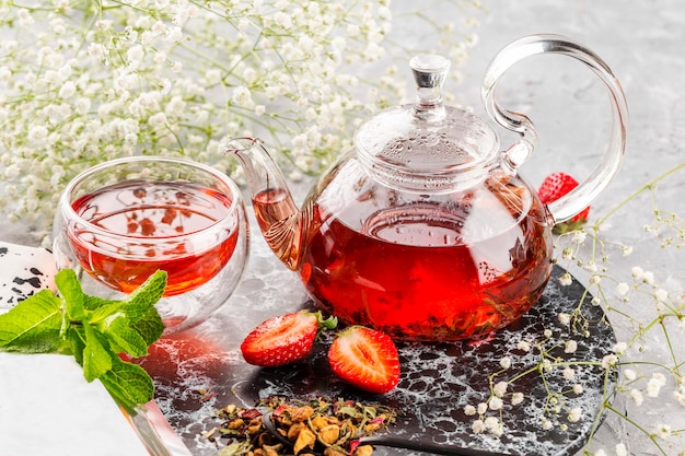 Hot red fruit tea in a glass teapot on a light background decorated with fresh mint