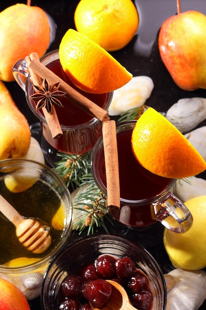 Hot red mulled wine bee honey slices of oranges and spices on a dark background Christmas decoration with spruce branches Closeup