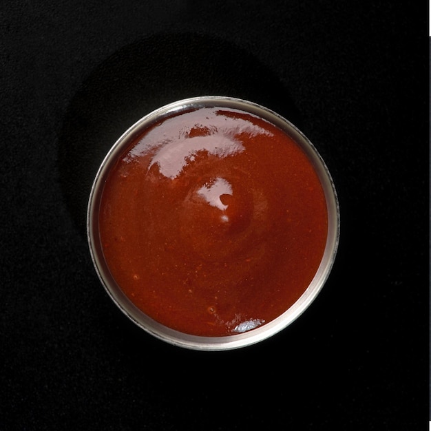 Hot sauce in a metal gravy boat on a black background for fast food