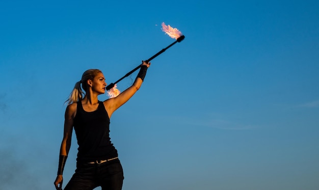 Hot and sexy Sensual girl twirl fire baton Pretty girl manipulate flaming rod outdoors Female fire performer on blue sky Baton twirling Holiday celebration Night party copy space