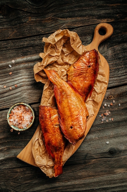 Hot smoked river bass fish on wooden cutting board. vertical image. top view. place for text.