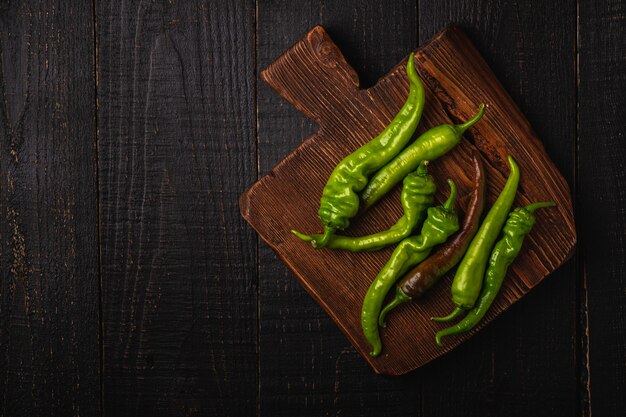 Hot spicy green chili peppers on teak wooden cutting board