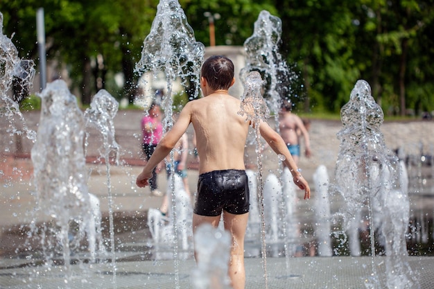 Hot summer weather unknown small children bathe in the city fountain in the park