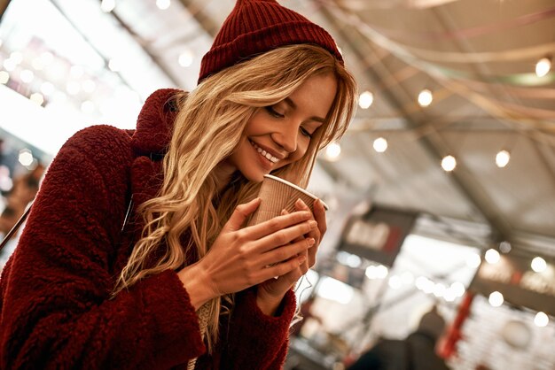 Hot sweet mulled wine. Close-up of woman drinking mulled wine at the street fair market. Cold season. Close-up photo of blonde woman