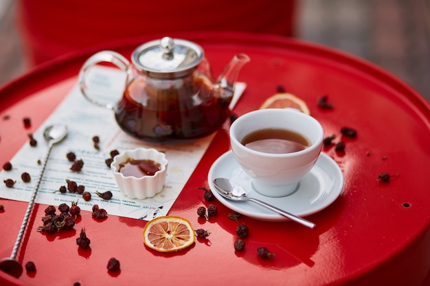 Hot tea in glass teapot and cup, on red background