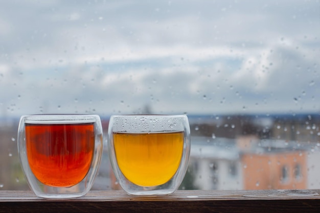 Hot tea in thermo glass on background window with raindrops