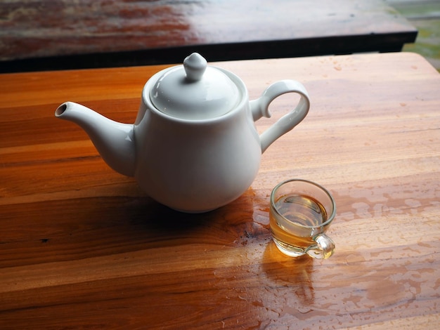 Hot tea in transparent glass cup and teapot on wet wooden table