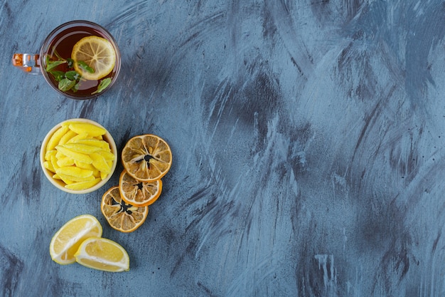 Hot tea with lemons and yellow bowl of yellow candies on blue background. 