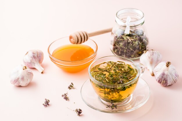 Hot tea with oregano in a cup, honey in a bowl, heads of garlic and dry herb in a jar. Herbal medicine and alternative therapy