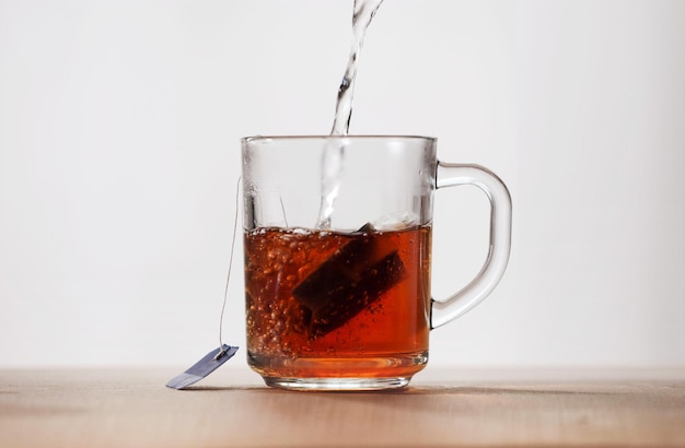 Hot water is poured into a glass mug with a tea bag Frontal view