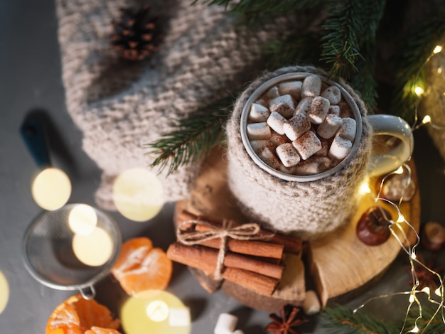 Hot winter drink chocolate, cocoa or coffee with marshmallows on the table in a knitted mug with cinnamon