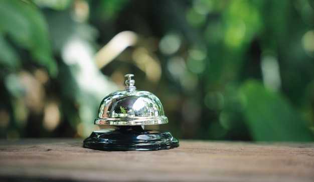 Hotel ring bell Closeup of silver service restaurant bell on wooden counter desk vintage bell to call staff outdoor in garden with green leaf