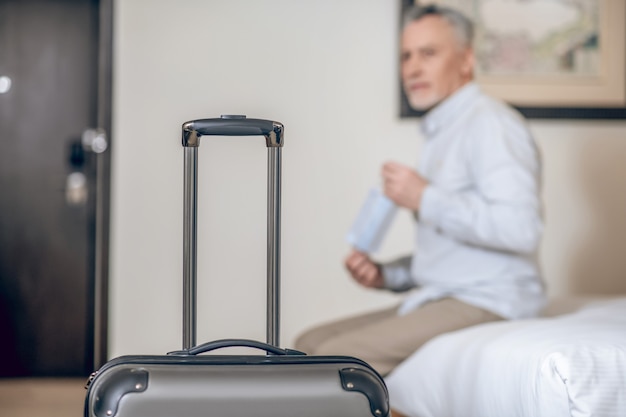 In the hotel room. Gray-haired mid-aged man with a protective mask in a hotel room