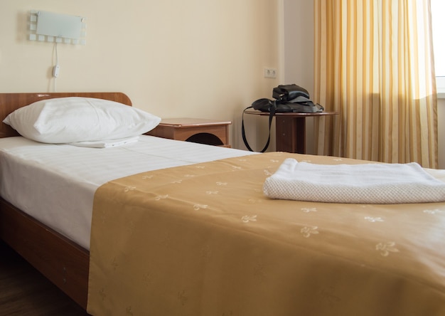 Hotel single Room with a bed, an armchair and a table with men's black bags.