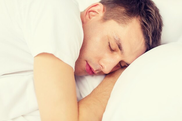 hotel, travel and happiness concept - handsome man sleeping in bed