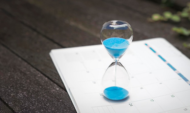 Hour glass and calendar on dark wood background