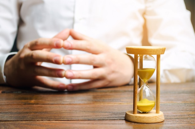 An hourglass and businessman holds his hands 