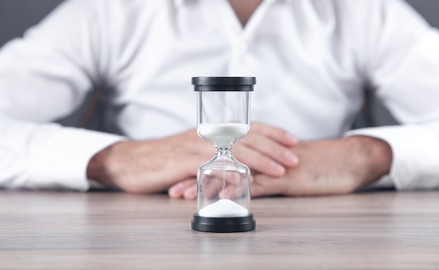 Hourglass on the desk with a man sitting in office.