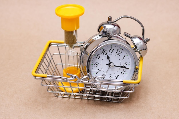 An hourglass and a metal alarm clock in the shopping basket. concept of time.