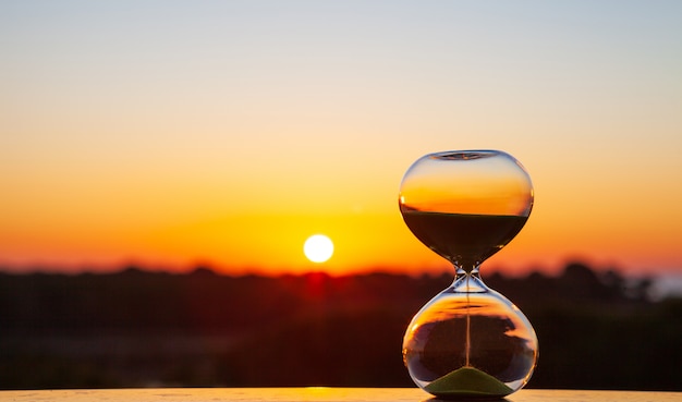 Photo hourglass at sunset or dawn on a blurry background, as a reminder of the passing time