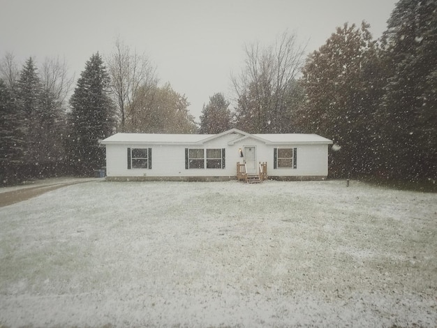 Photo house by trees against sky during snowfall