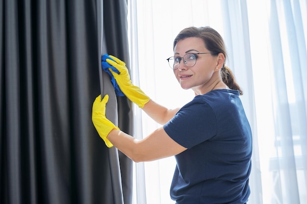 House cleaning woman in gloves with a rag cleaning curtains Housework housekeeping household cleanliness concept