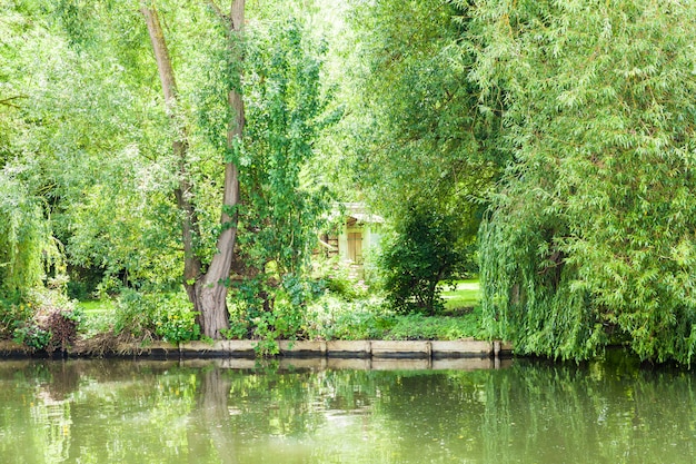 House hidden in vegetation trees and flowers at the edge of a canal in summer.