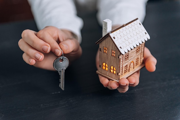 House keys in the hands of a woman and a small model of a house with luminous windows nearby. concept of acquiring your home