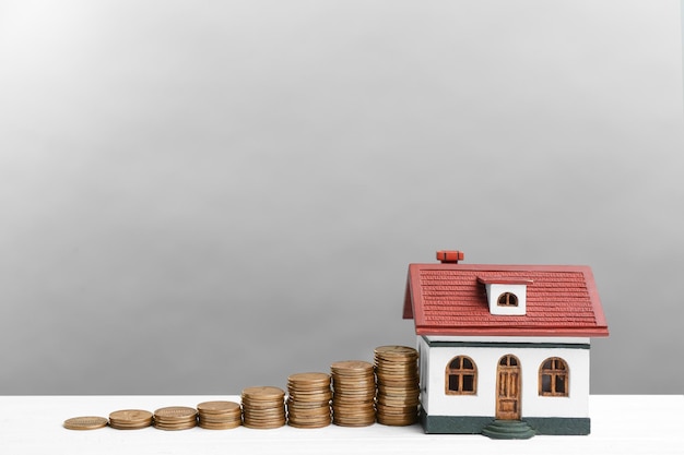 House model and coins on white wooden table against light grey background Money savings