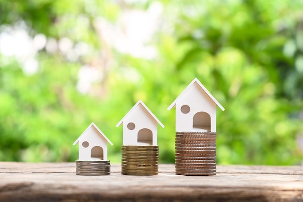 House model on pile of coins and blurred natural green background