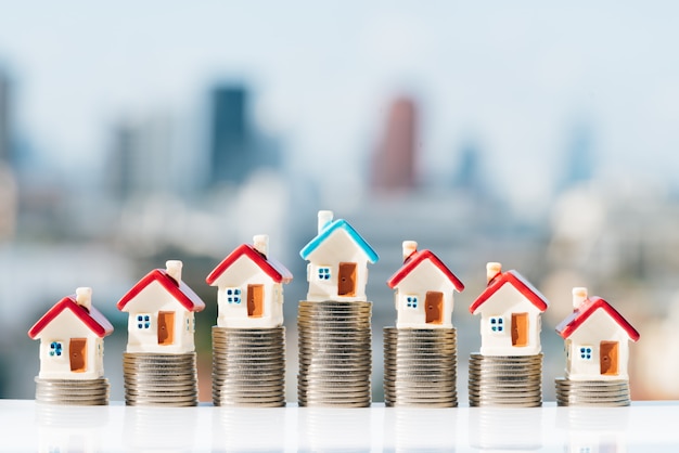 House models on top of coins stack with city backgrounds. 