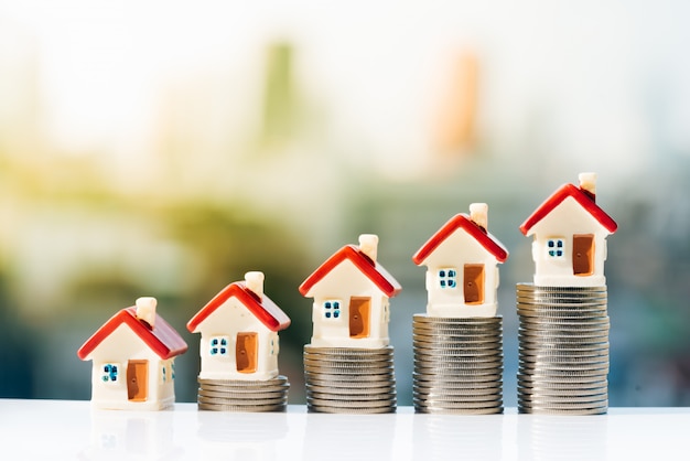 House models on top of coins stack with city backgrounds. 