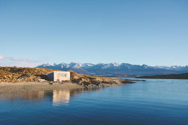 House on river with mountains at back.