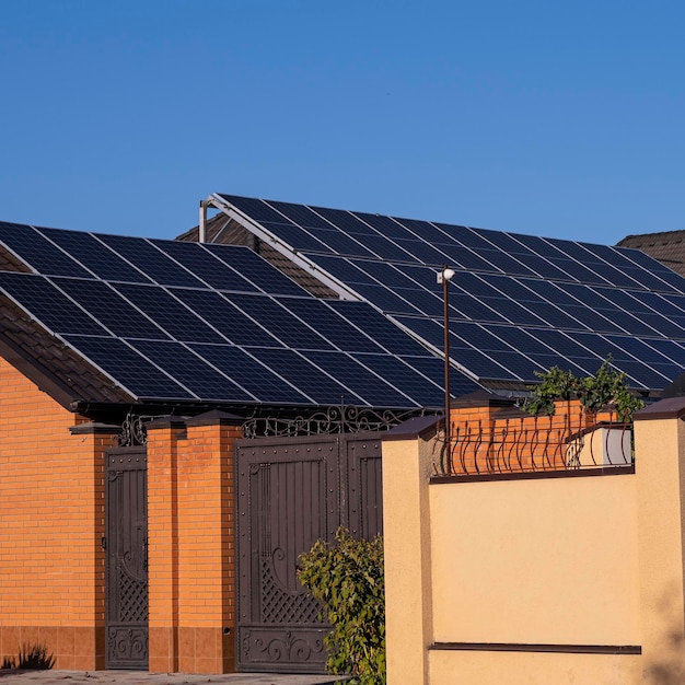 House with a brown metal roof and solar panels. Fence and house made of stone.