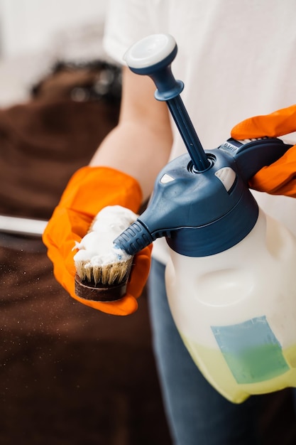 Housekeeper is pouring detergent on brush for dry cleaning using extractor machine Process of dry cleaning for removing stains and dirt from couch at home Professional cleaning service