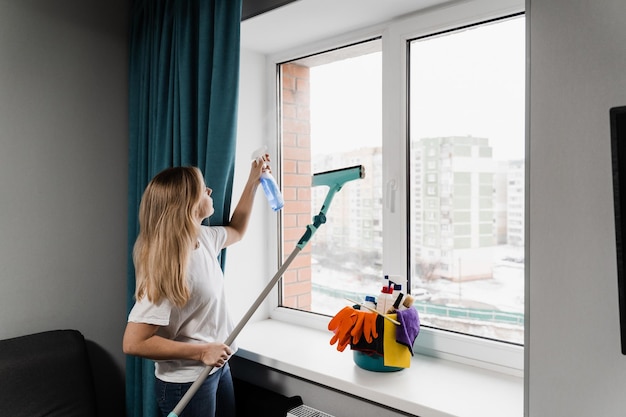 Housekeeper is spraying detergent and cleaning window at home Housewife woman is cleaning at home and washing windows House cleaning service