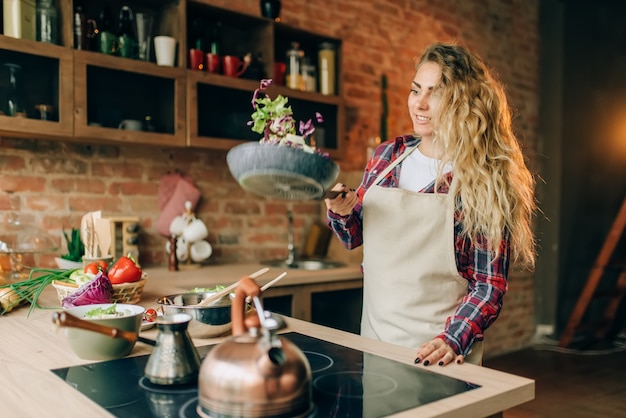 Housewife in apron frying vegetables in a pan