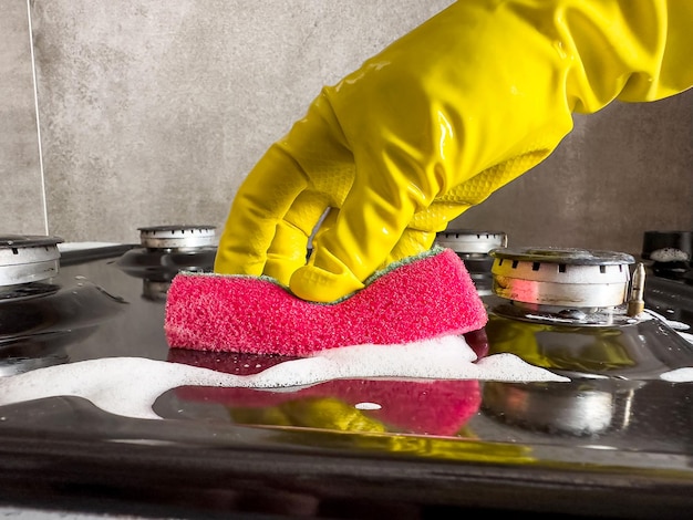 Housewife cleaning dirty gas stove from grease with sponge rag in home kitchen