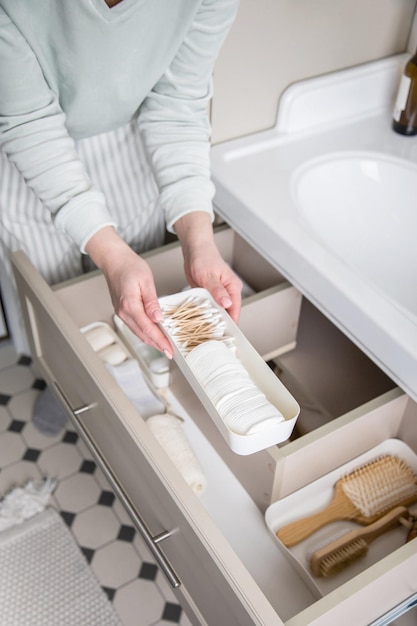 Housewife hands putting rolled up towel into drawer under sink organizing storage space in bathroom